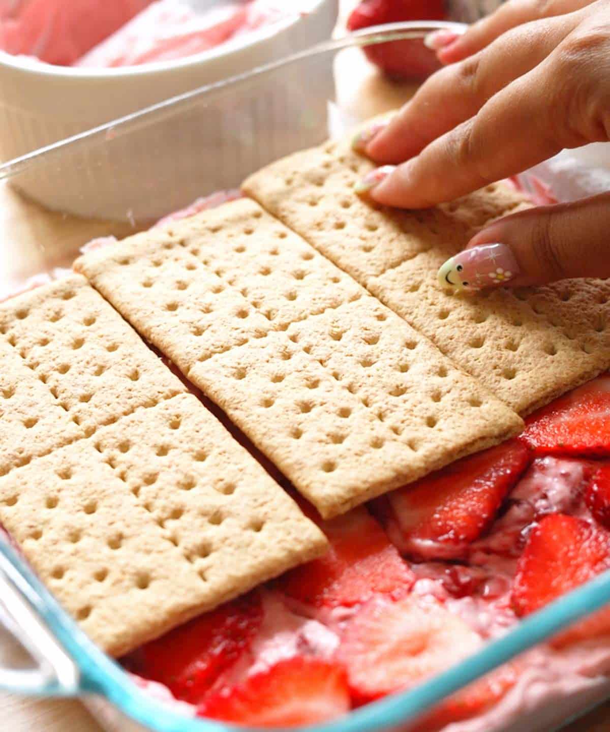 Adding a layer of graham crackers on top of sliced strawberries.