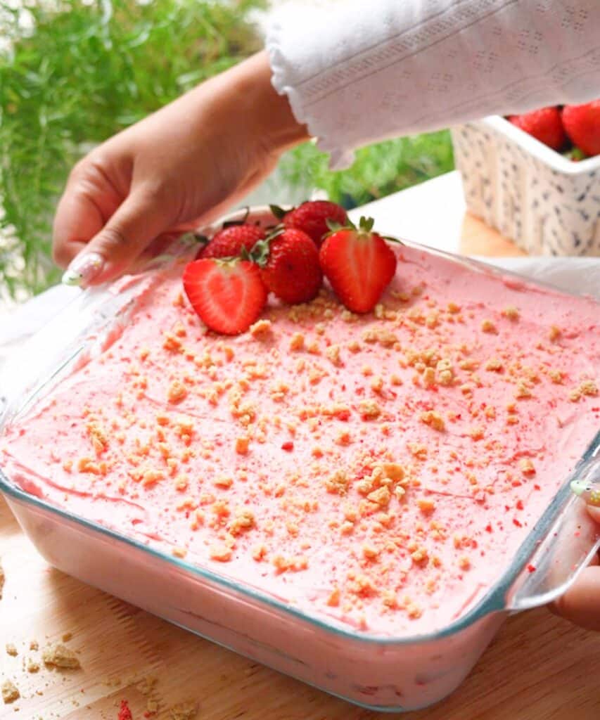 Holding glass square dish of triple strawberry icebox cake.