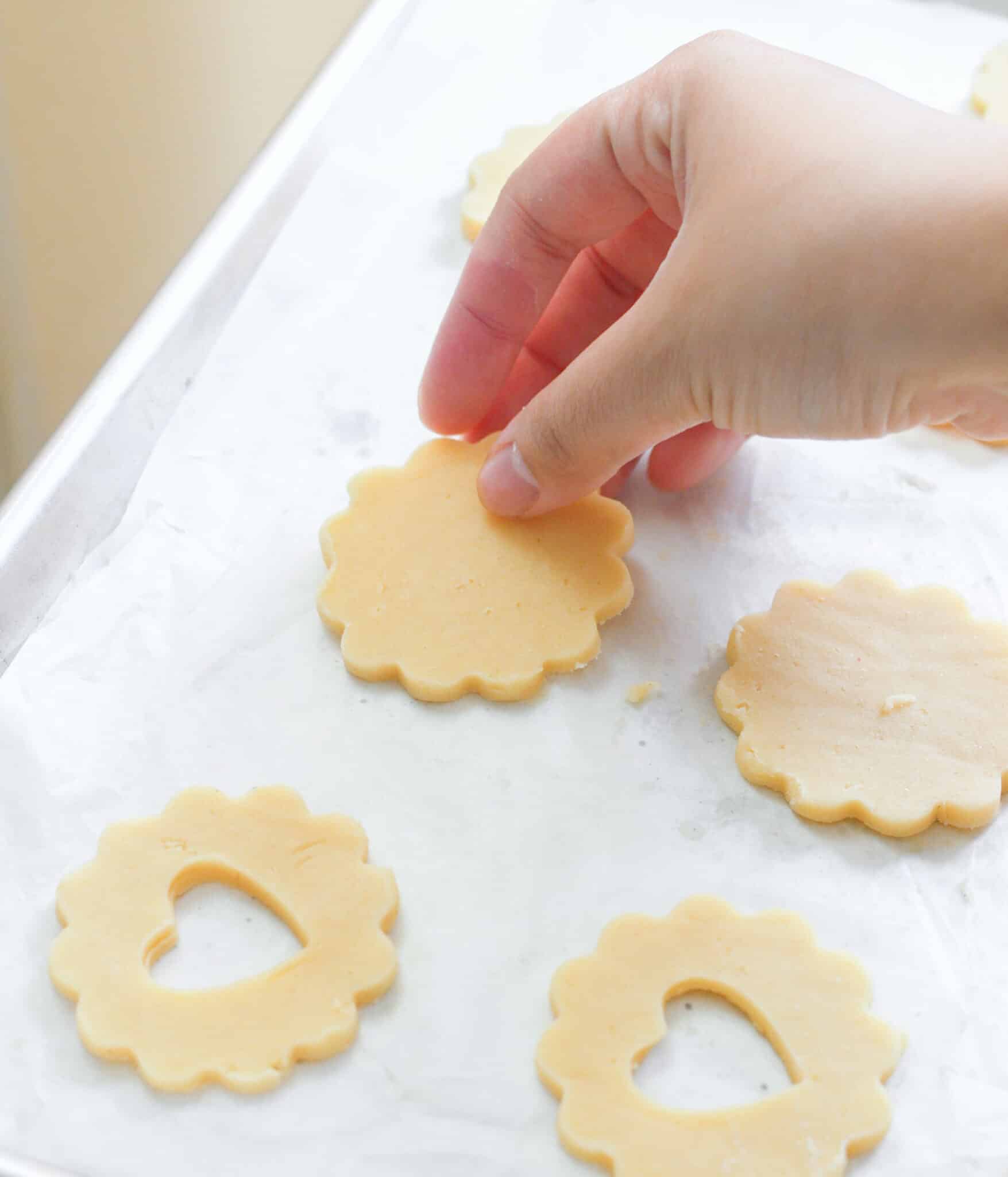 Placing cut out linzer cookies on lined baking sheet.