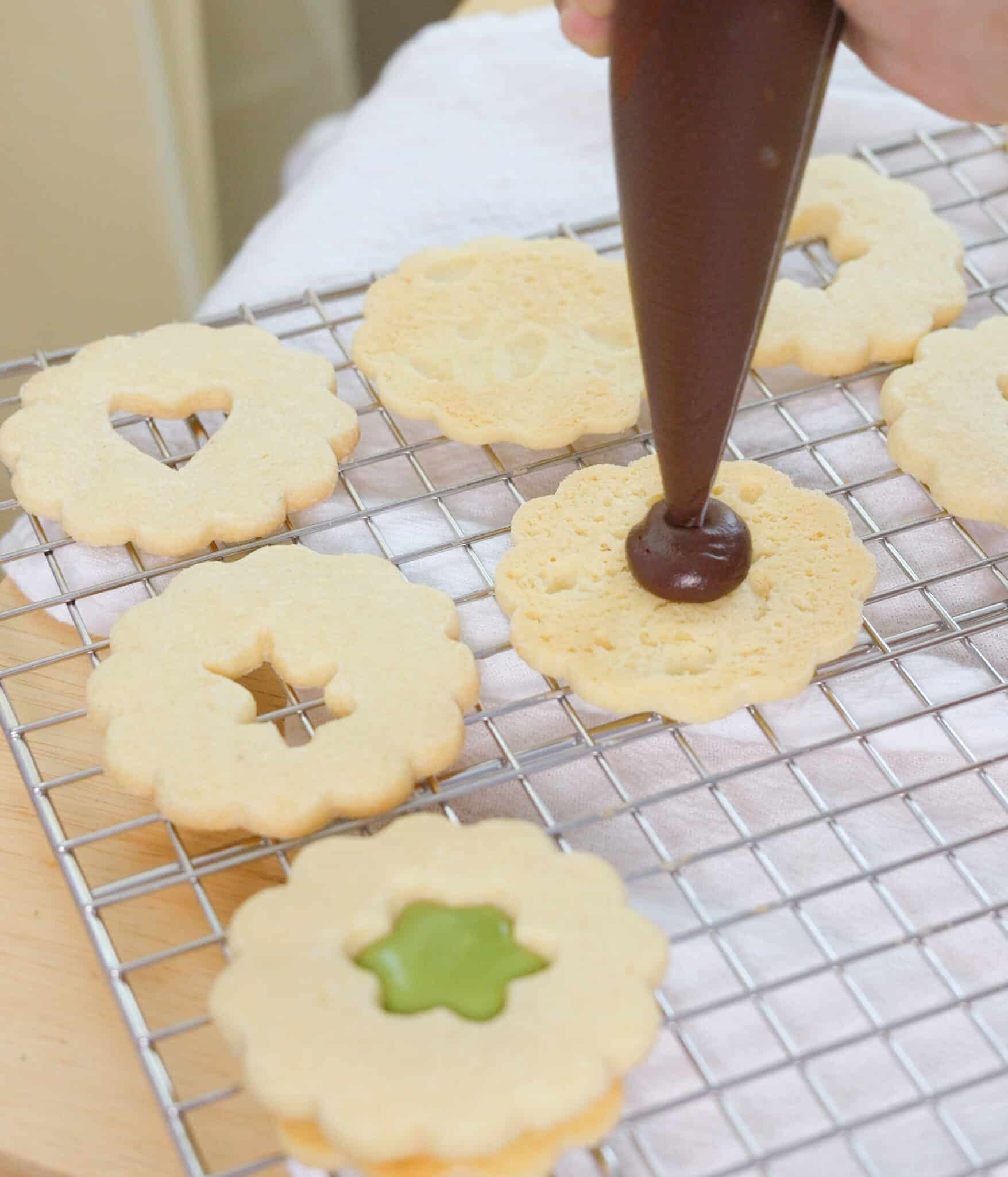 Piping ganache onto freshly baked linzer cookie.