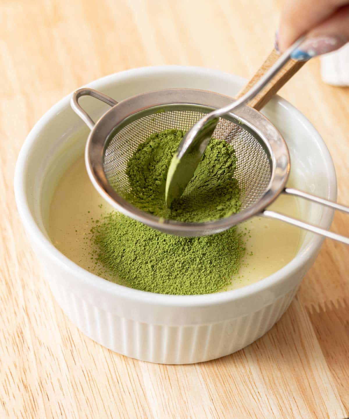 Sifting culinary matcha powder into melted white chocolate and heavy cream mixture.