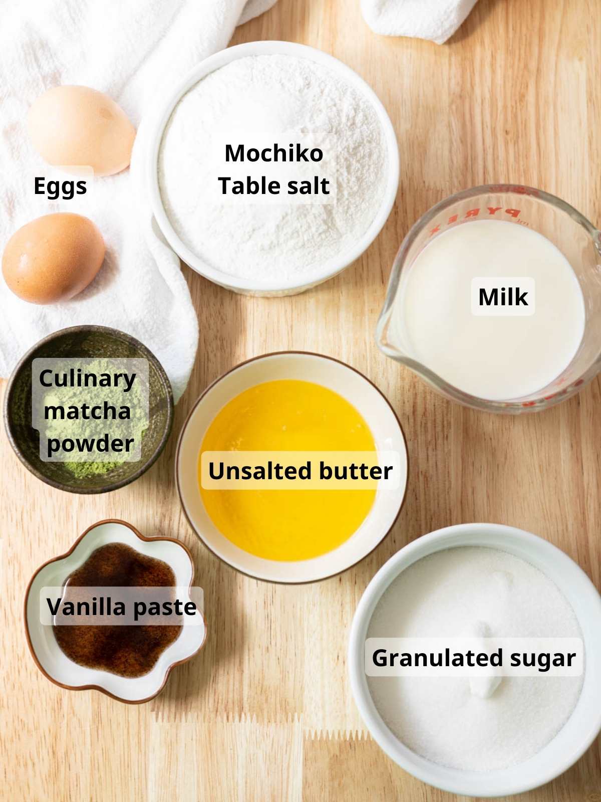 Matcha mochi brownies ingredients laid out on a wooden table, with labels for each ingredient.