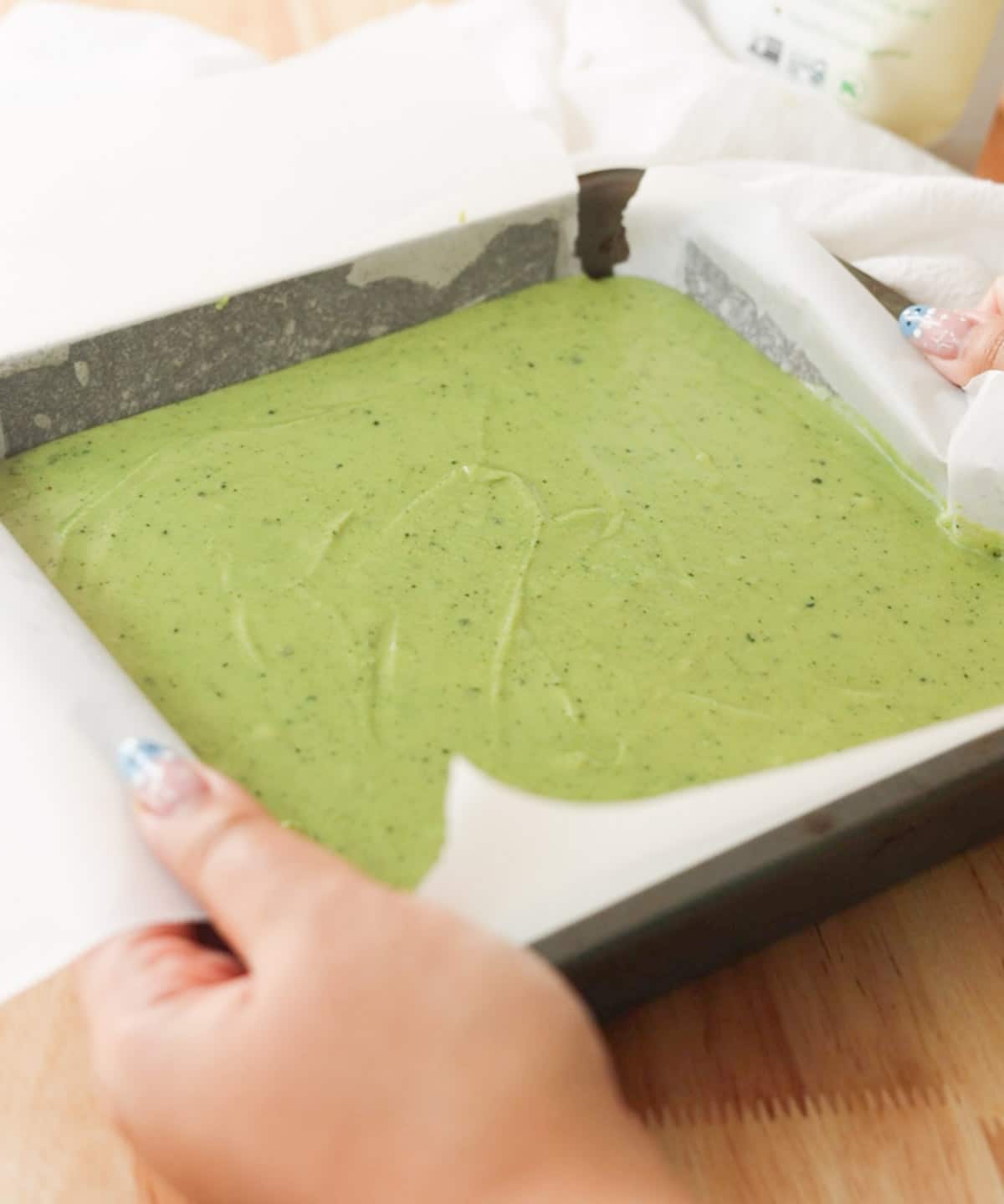 Holding a square metal baking tray with matcha mochi brownie, ready to be baked.