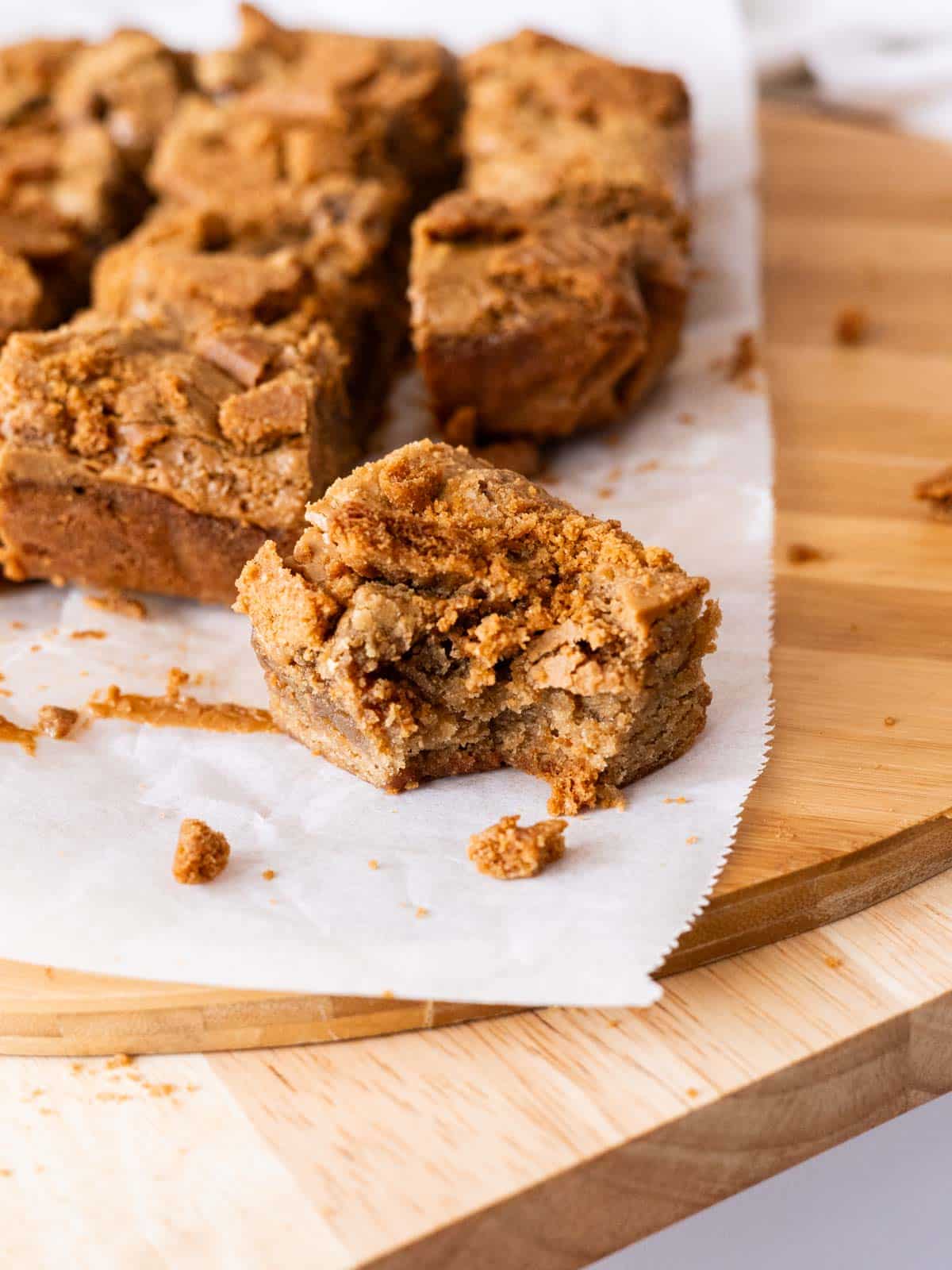 Biscoff blondie bars with a bite taken out of it, on top of parchment paper.