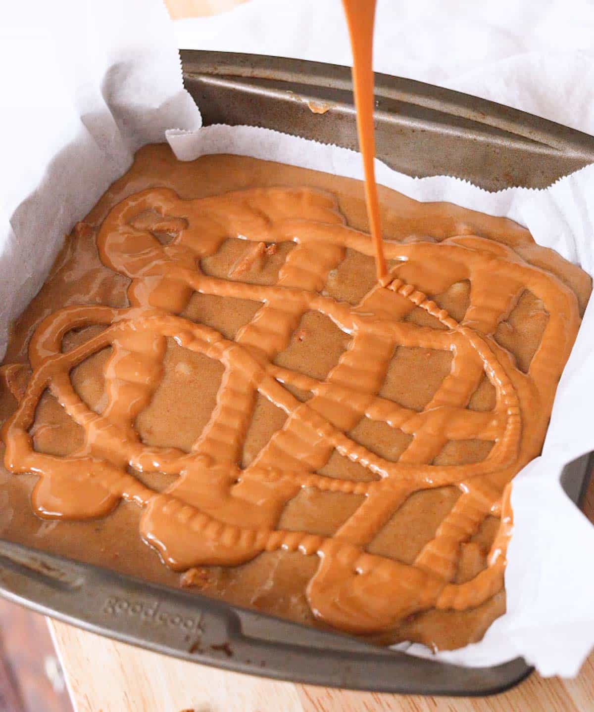 Pourring Biscoff spread on top of blondie batter in lined square baking pan.