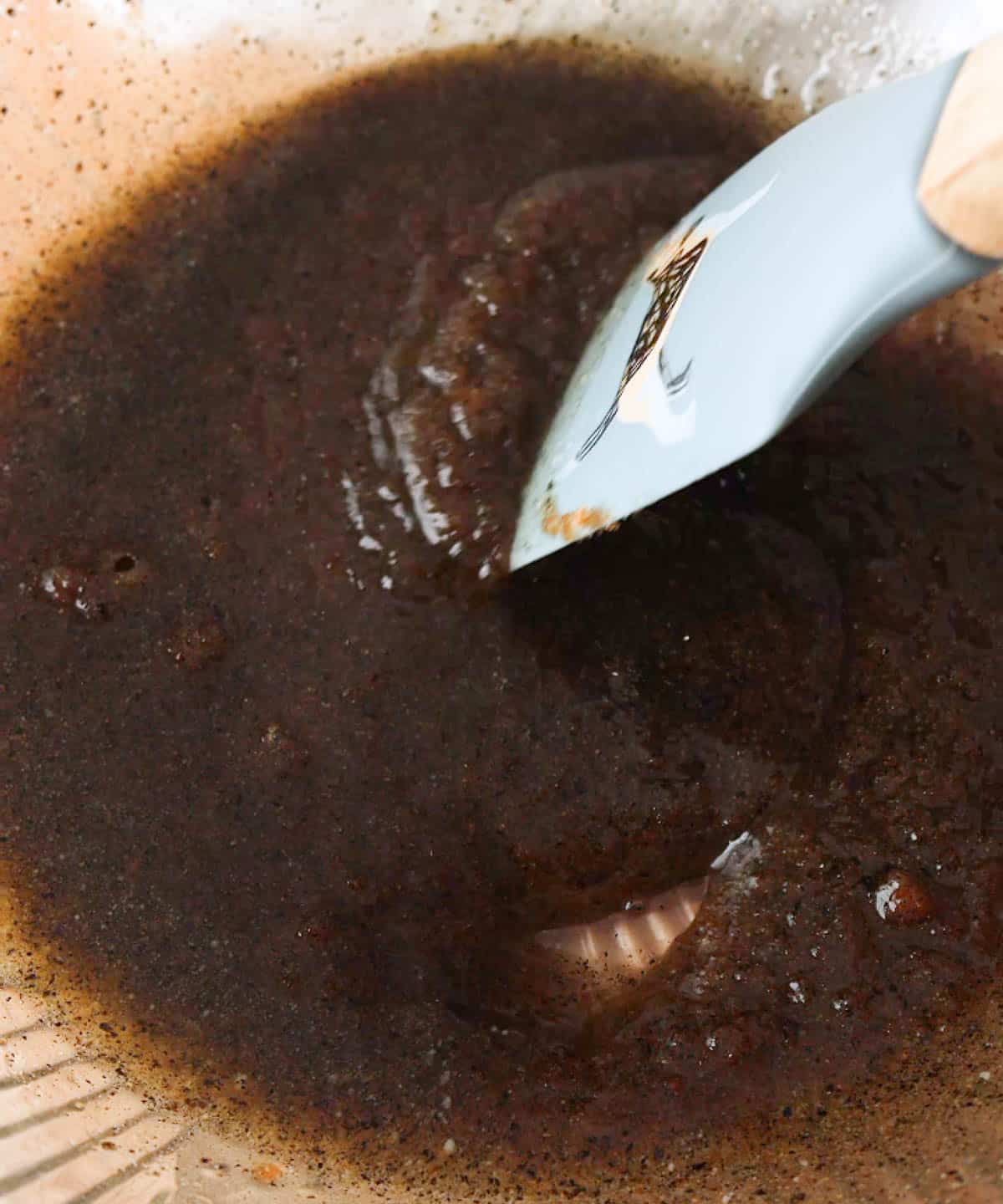 Mixing sugars, black sesame powder, and melted butter in a glass mixing bowl with a spatula.