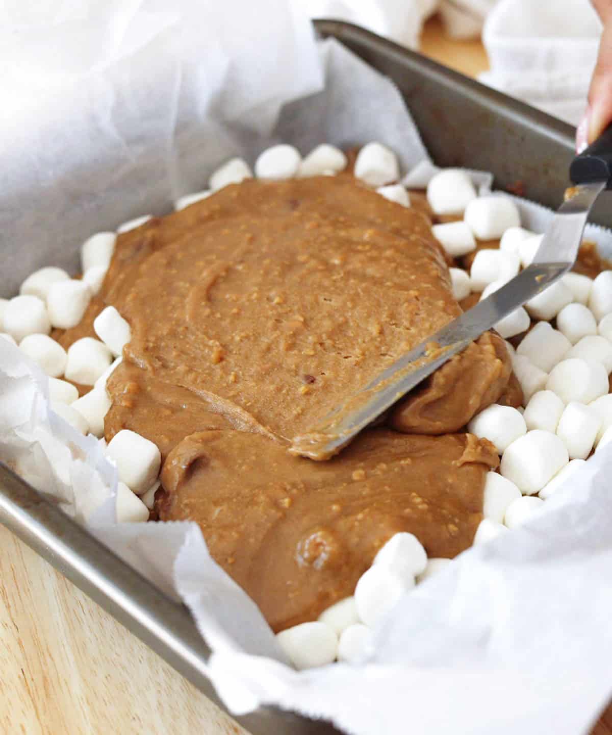 Spreading blondie batter on top of a layer of marshmallows in baking pan.