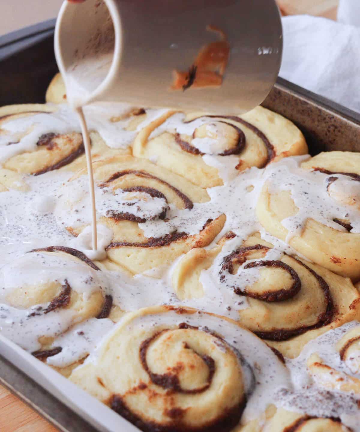 Pouring spiced heavy cream mixture on top of fully proofed cinnamon rolls.