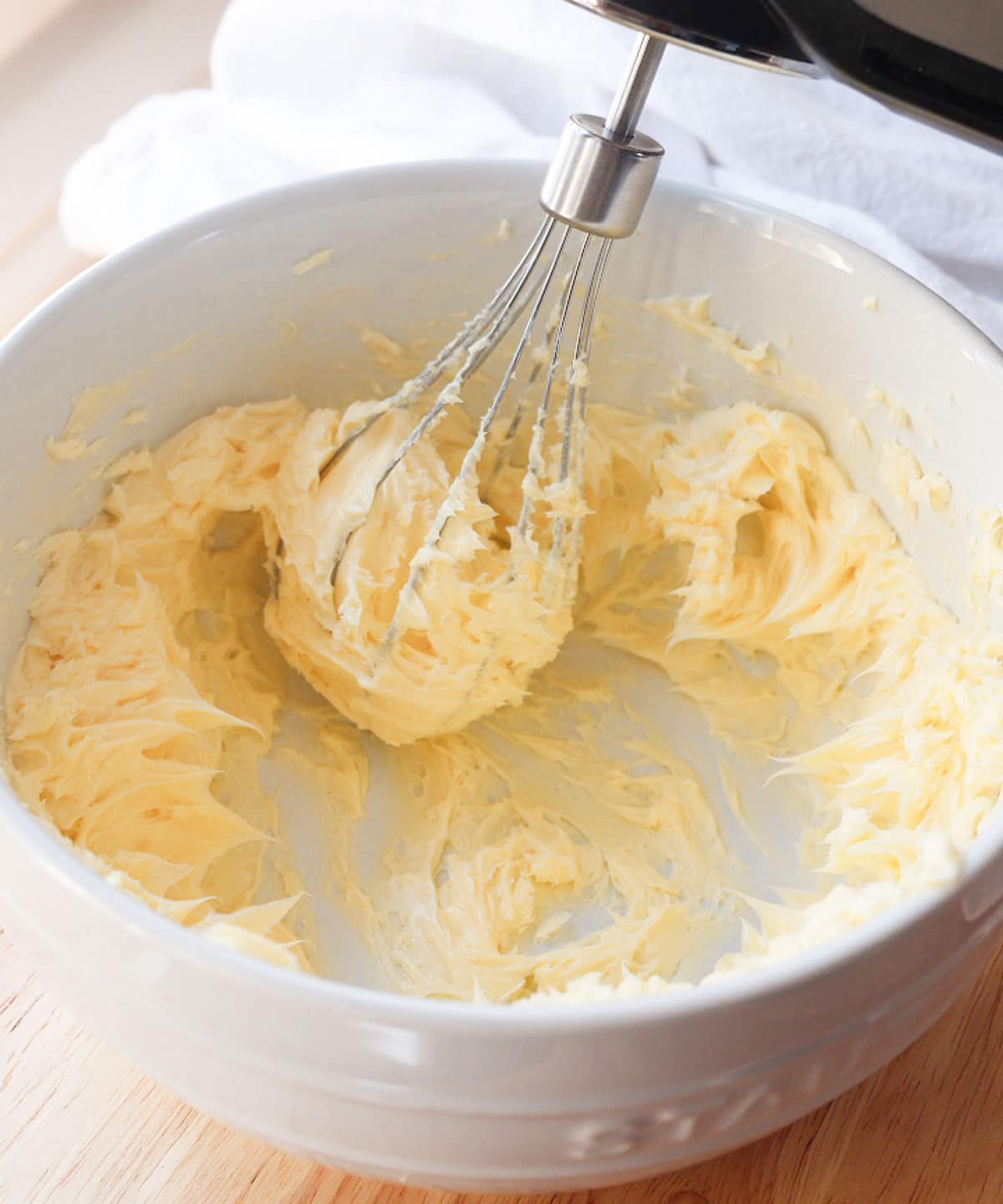 Whipping softened honey with electric mixer in white mixing bowl.