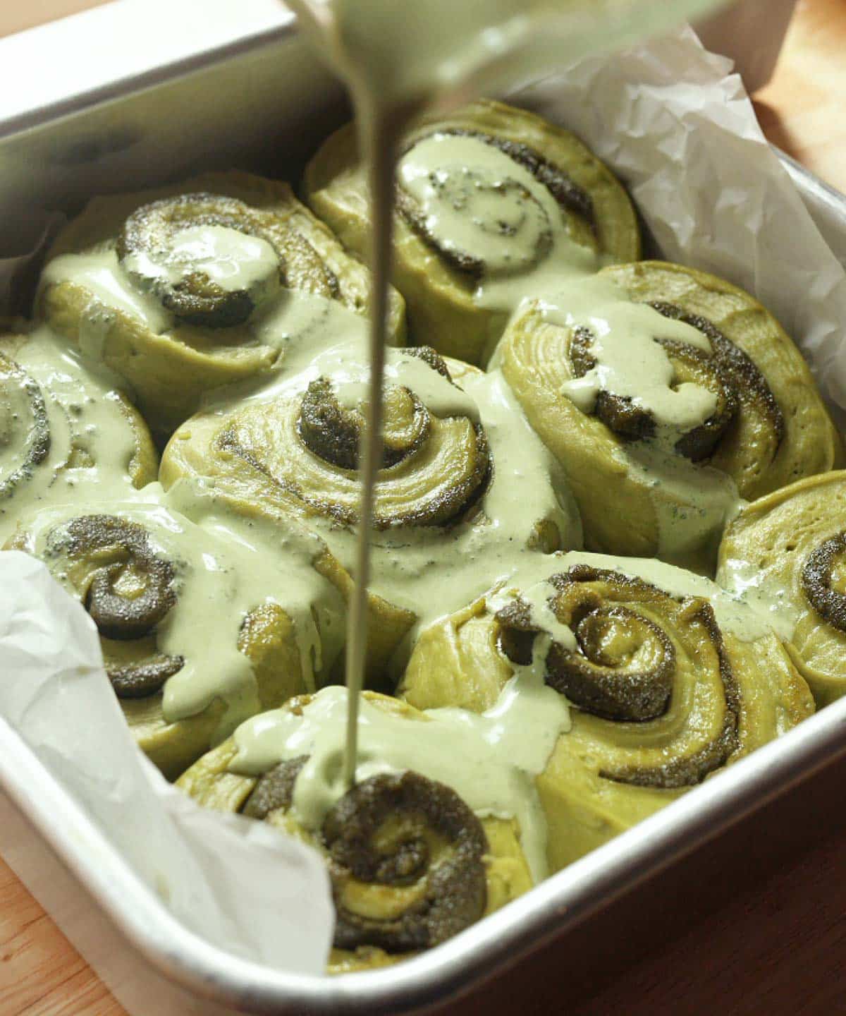 Pouring matcha heavy cream mixture on top of fully proofed matcha buns.