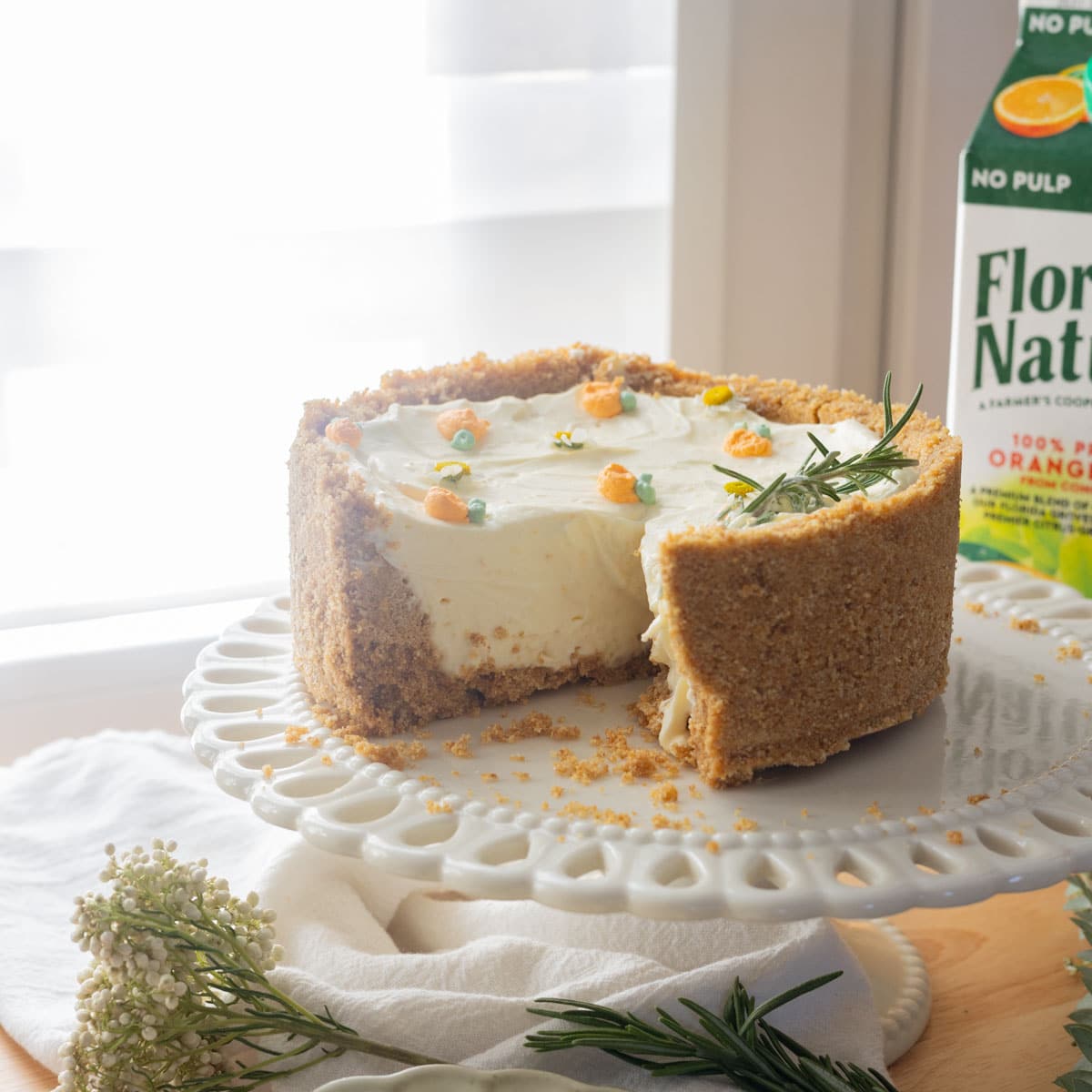 No bake orange cheesecake on a vintage white cake stand, with a slice taken out of it.