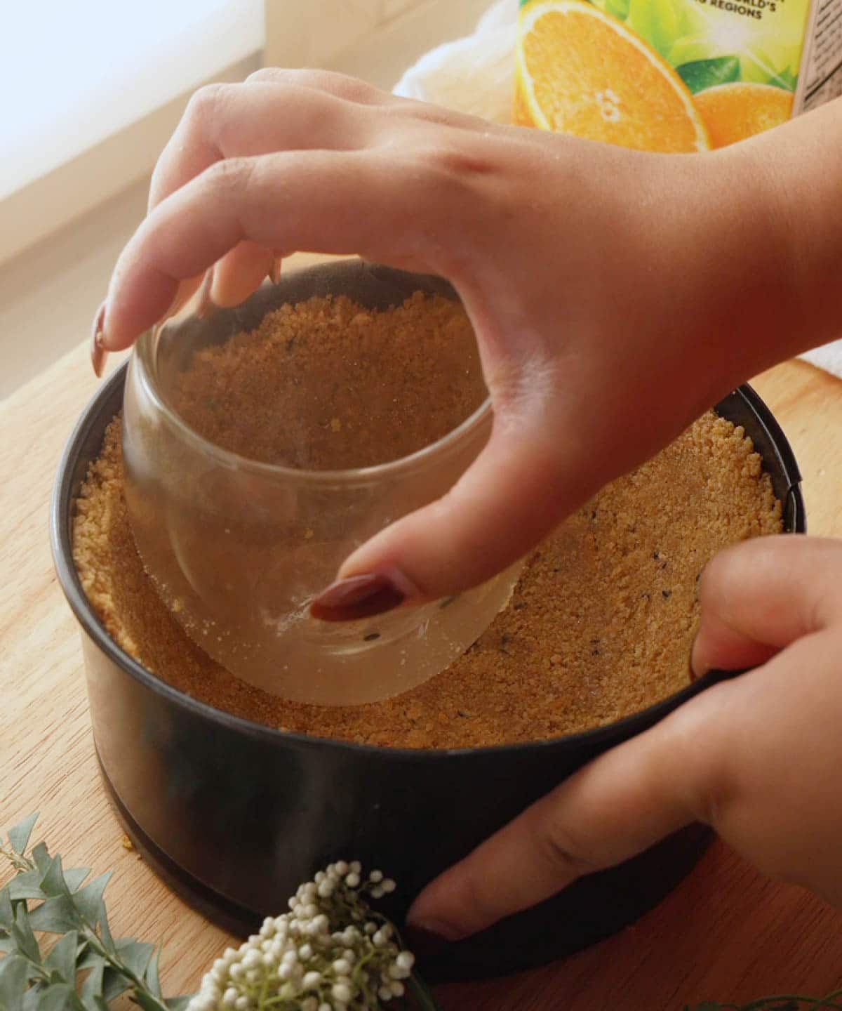 Using a cup to press graham cracker crust into springform pan.