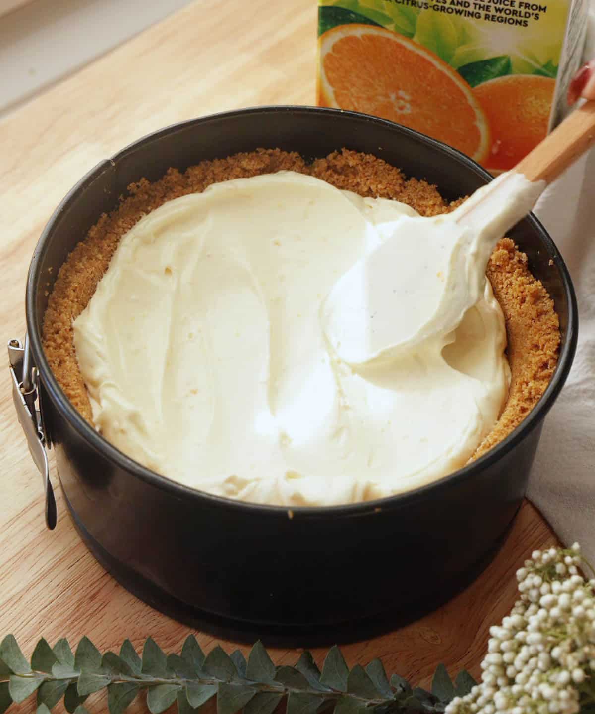 Using a spatula to smooth out orange cheesecake filling.