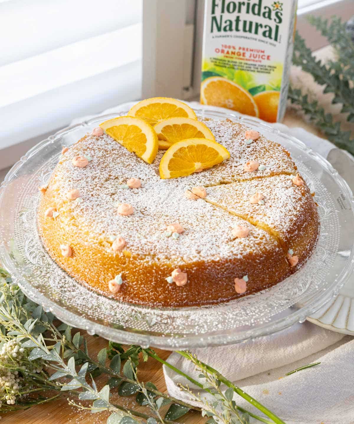 Orange olive oil cake decorated with powdered sugar, sliced oranges, and candy melts.