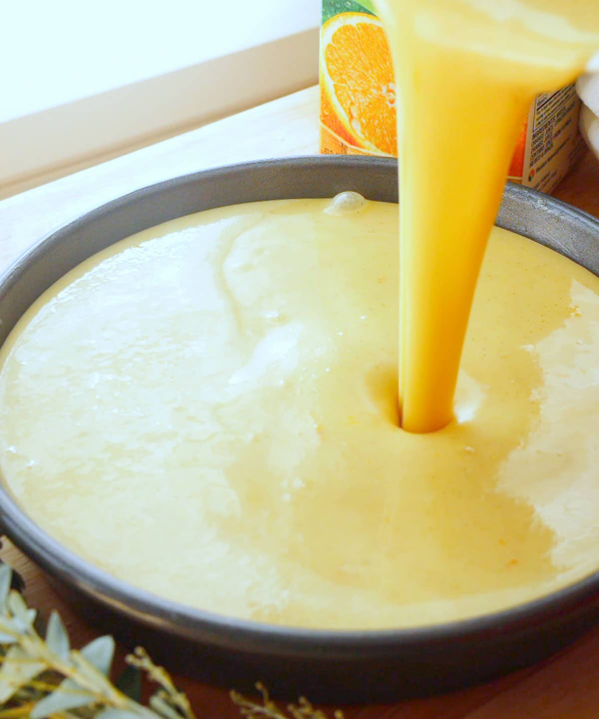 Pouring orange olive oil cake batter into cake pan.