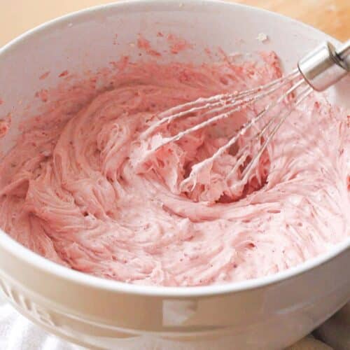 Pink strawberry frosting in a white mixing bowl.