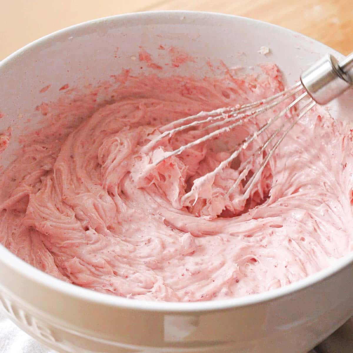 Pink strawberry frosting in a white mixing bowl.