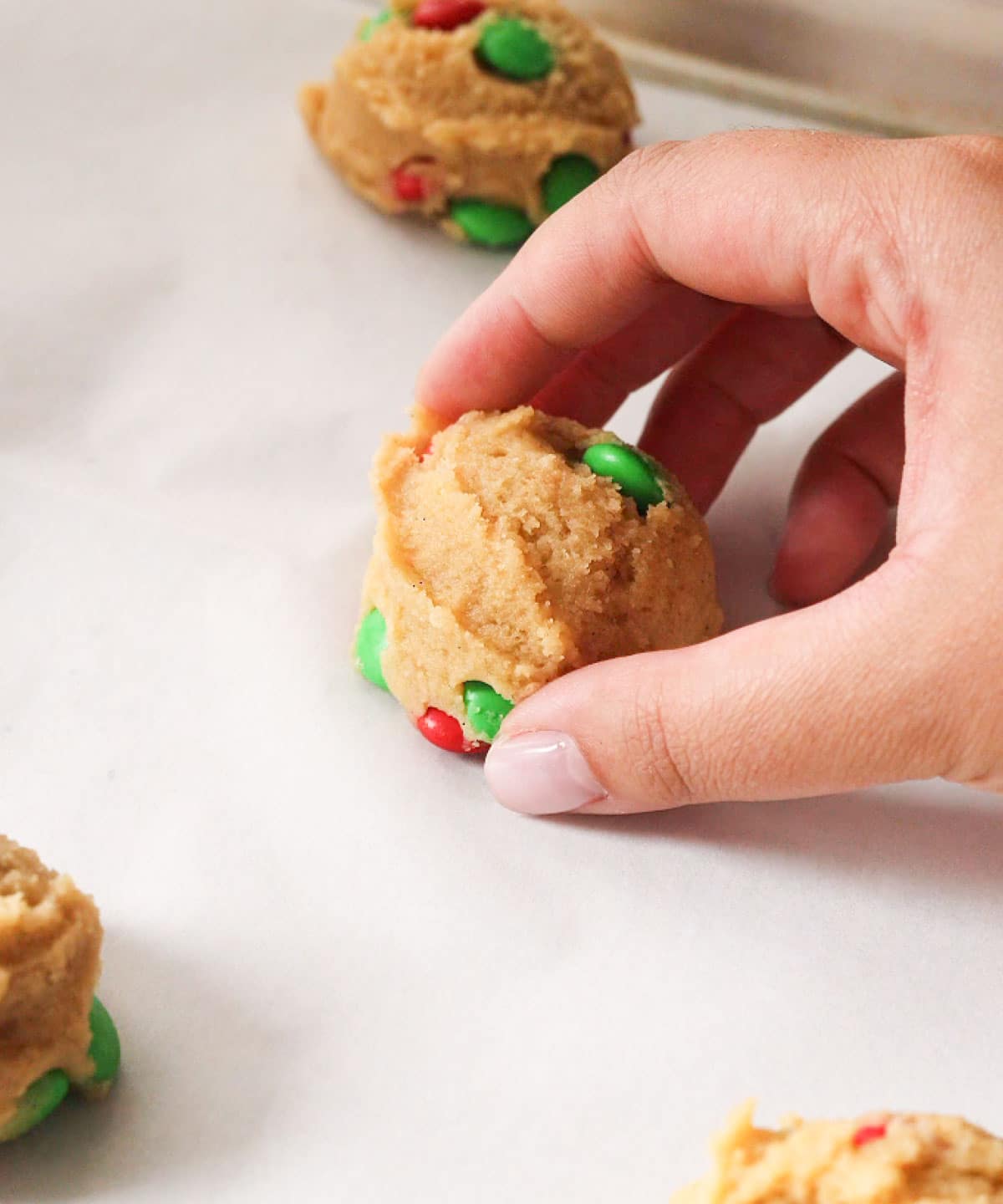 Placing raw M&M cookie dough ball on lined baking tray.