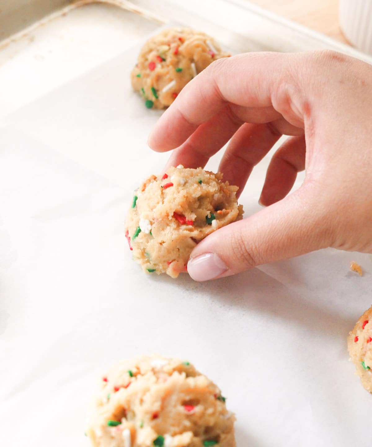 Placing raw Christmas sprinkle cookie dough ball on lined baking tray.