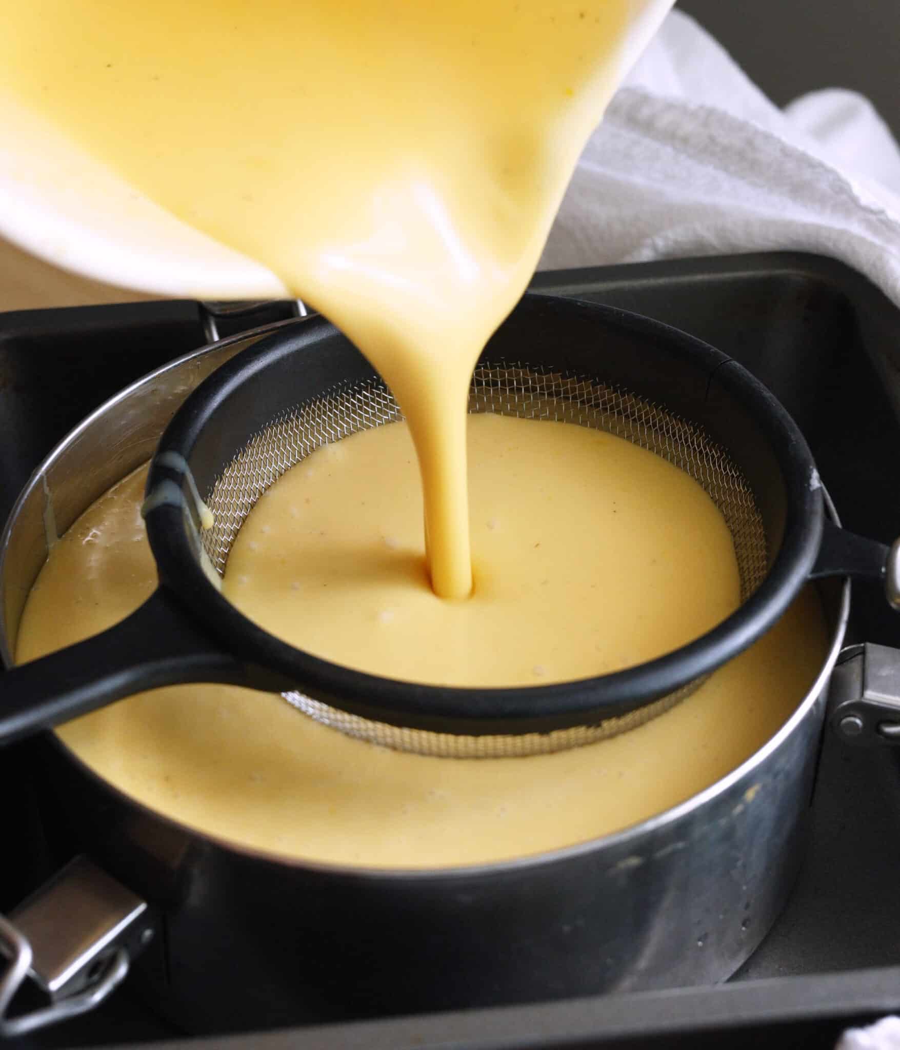 Pouring leche flan batter through sieve into baking pan.