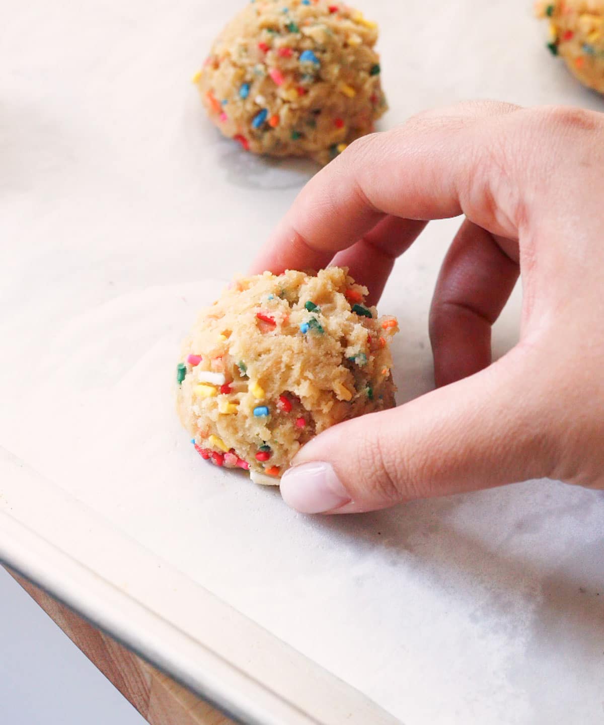 Placing a funfetti cookie dough ball on lined baking tray.