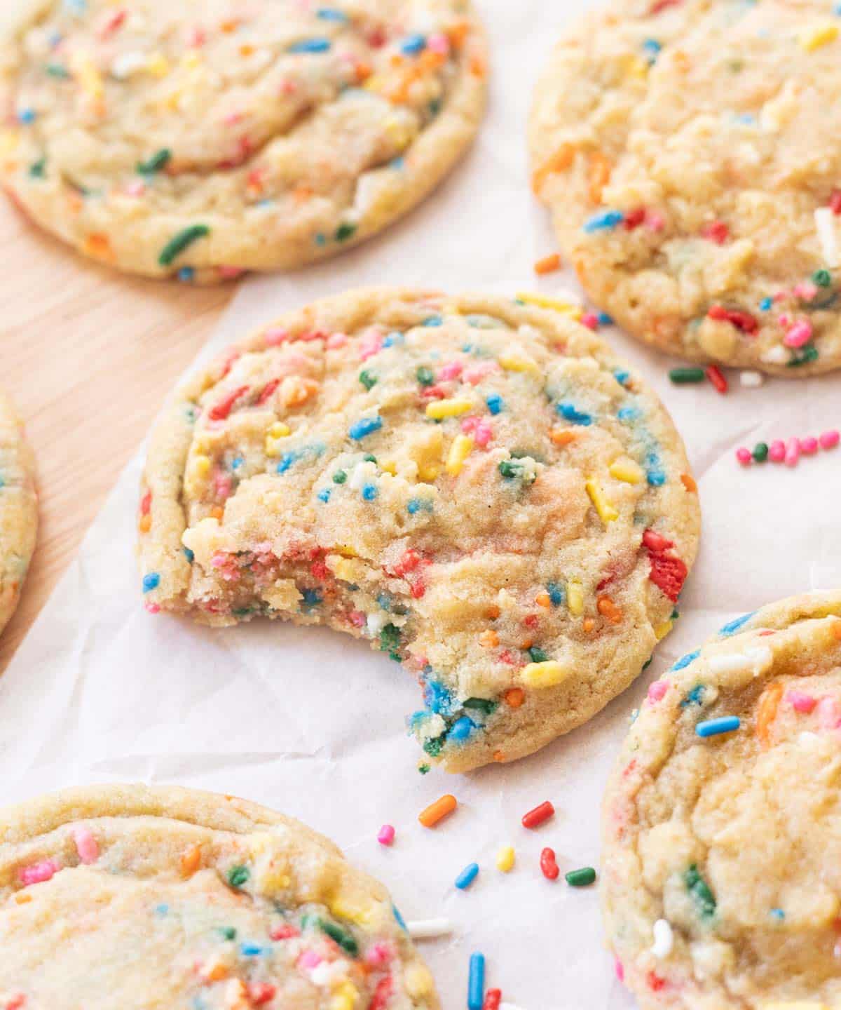 Funfetti sprinkle cookie with a bite taken out of it on white parchment paper.