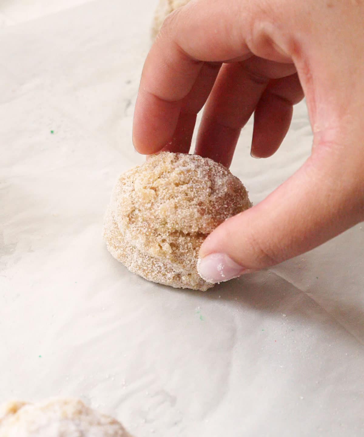 Placing a rolled sugar cookie dough ball onto a lined baking tray.