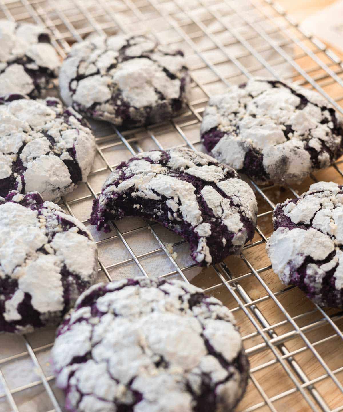 Ube crinkle cookies on a wire rack with a bite taken out of one.