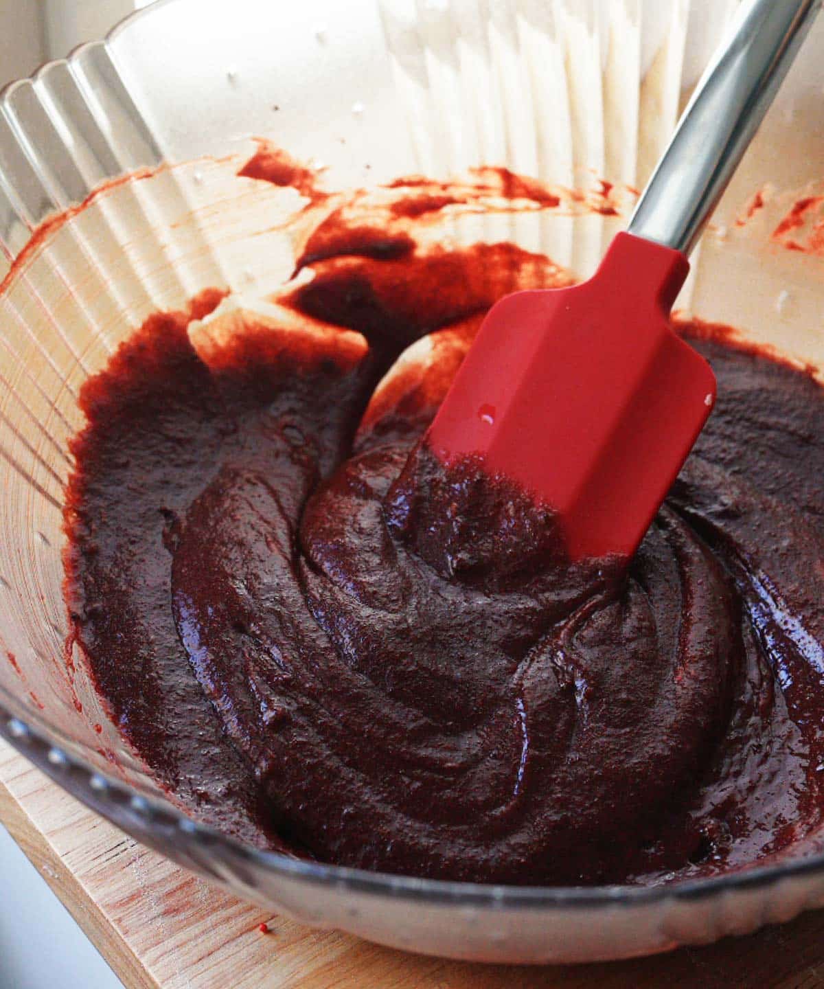 Wet ingredients mixed in a glass bowl, showing a dark red, thick, silky batter.