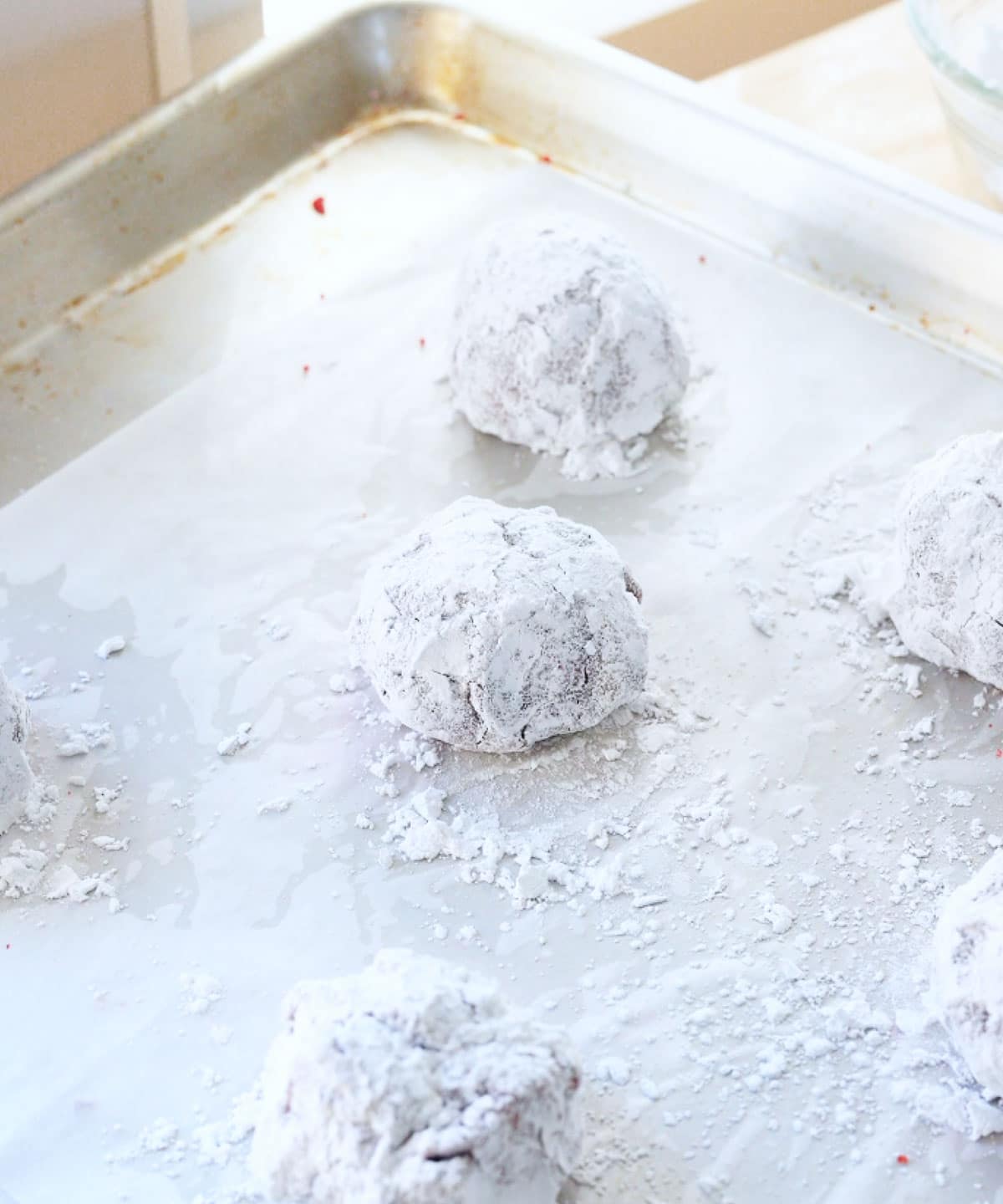 Red velvet crinkle cookie dough balls with a thick layer of powdered sugar, ready to be baked.