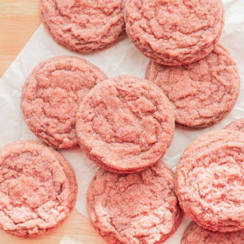 Pink strawberry sugar cookies laid out on parchment paper.