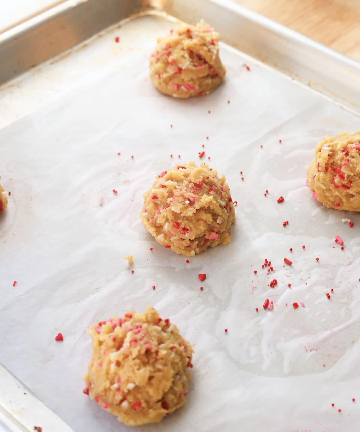 Heart sprinkle cookie dough balls on lined baking tray, ready for the oven.