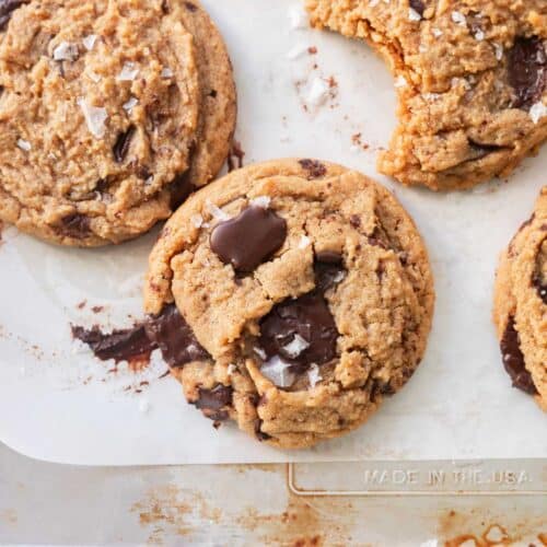 Peanut butter chocolate chip cookies topped with flaky sea salt on a lined baking tray.