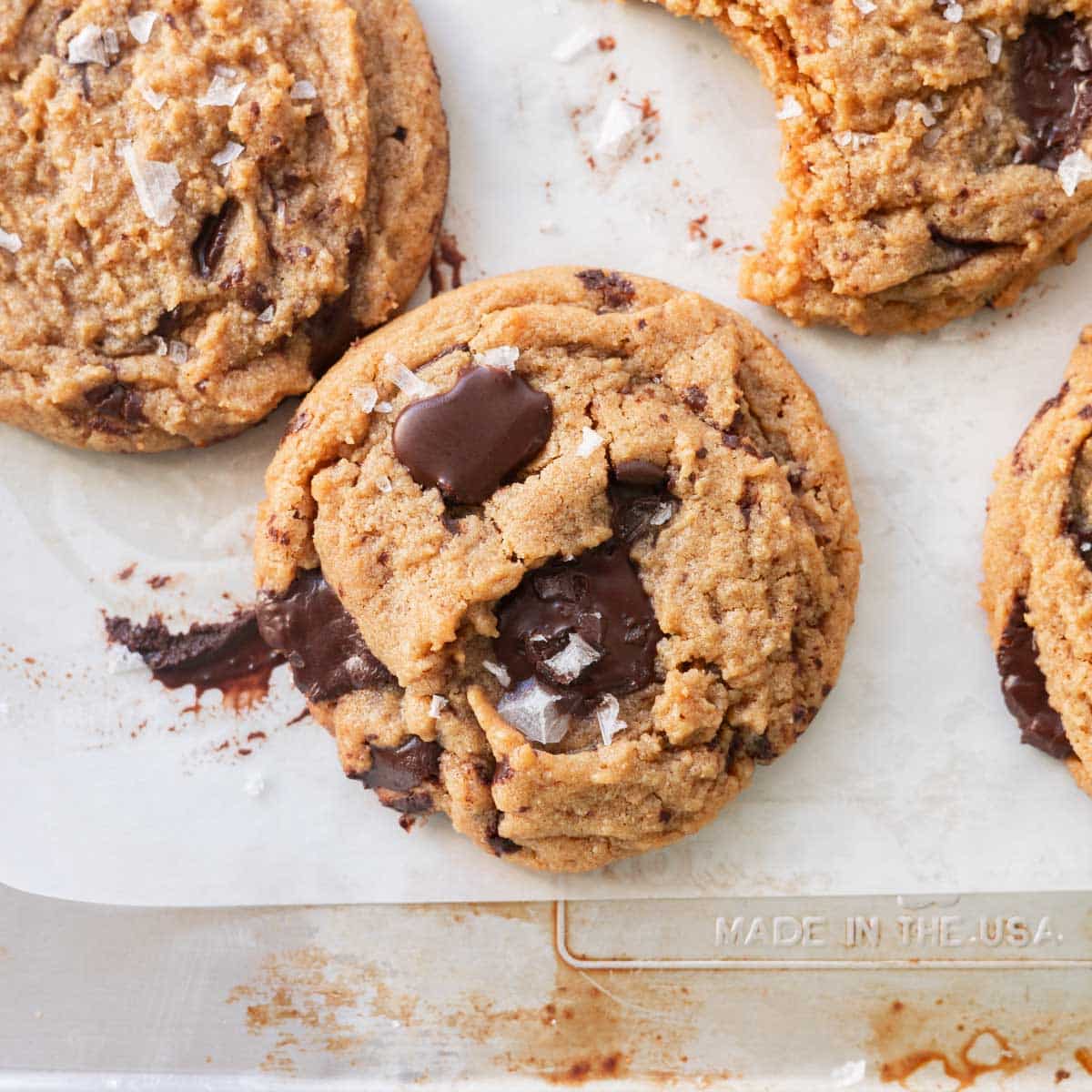 Peanut butter chocolate chip cookies topped with flaky sea salt on a lined baking tray.