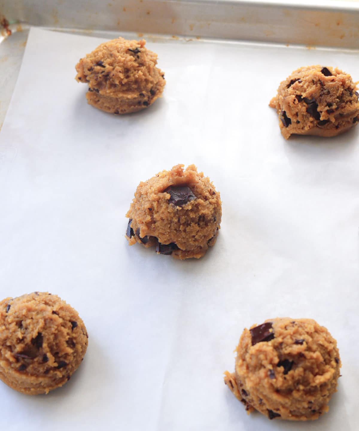 Peanut butter chocolate chunk cookie dough balls placed on a lined baking tray.