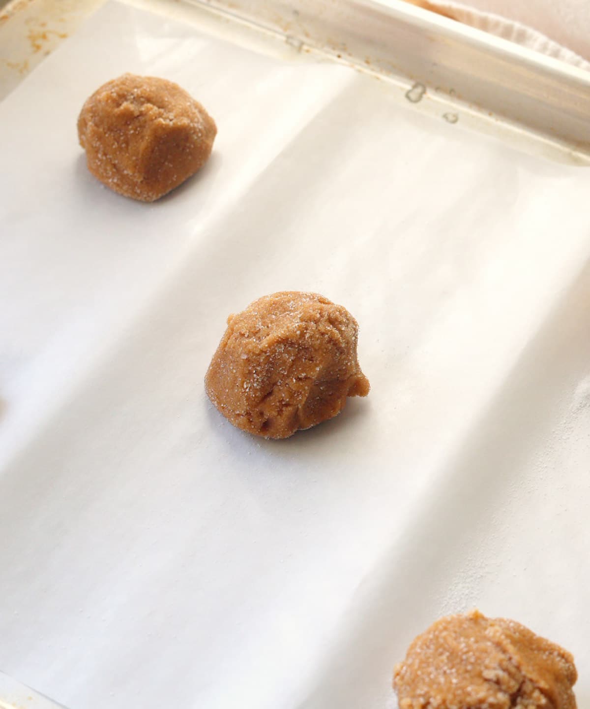 Peanut butter cookie dough ball rolled in sugar, placed on a lined baking tray.