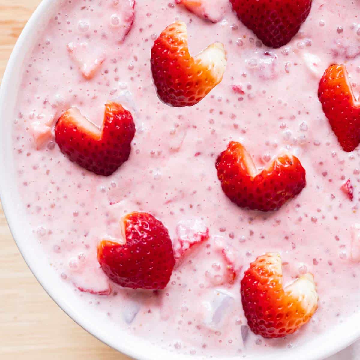 Pink strawberry sago topped with strawberry hearts in a white bowl.