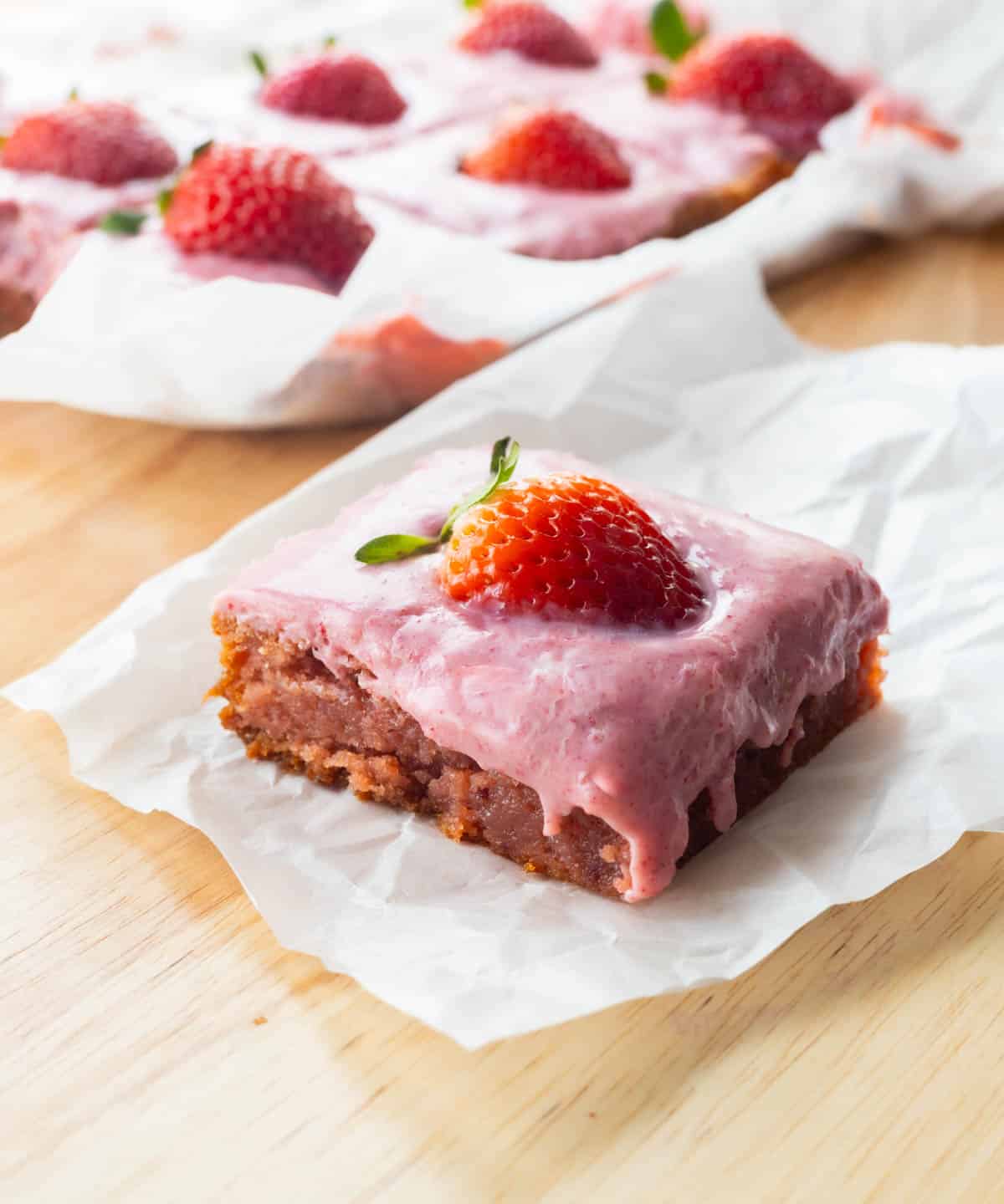 Strawberry brownie on parchment paper, topped with strawberry ganache and a fresh strawberry.