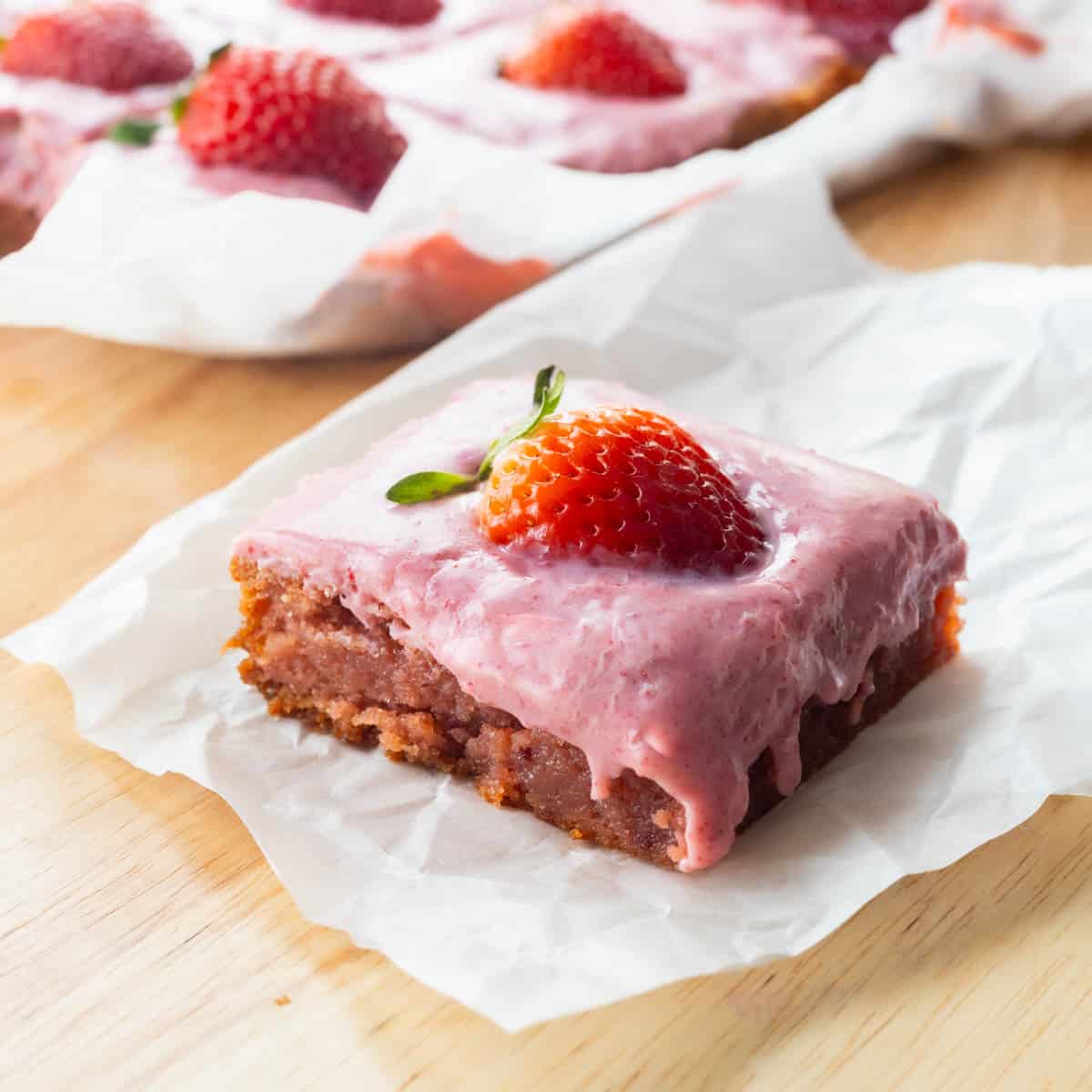 Strawberry brownie on parchment paper, topped with strawberry ganache and a fresh strawberry.