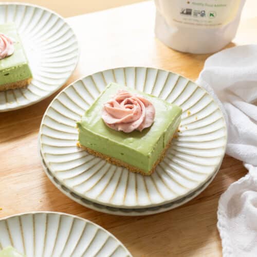 No bake matcha cheesecake bar topped with strawberry whipped cream on a fluted plate.