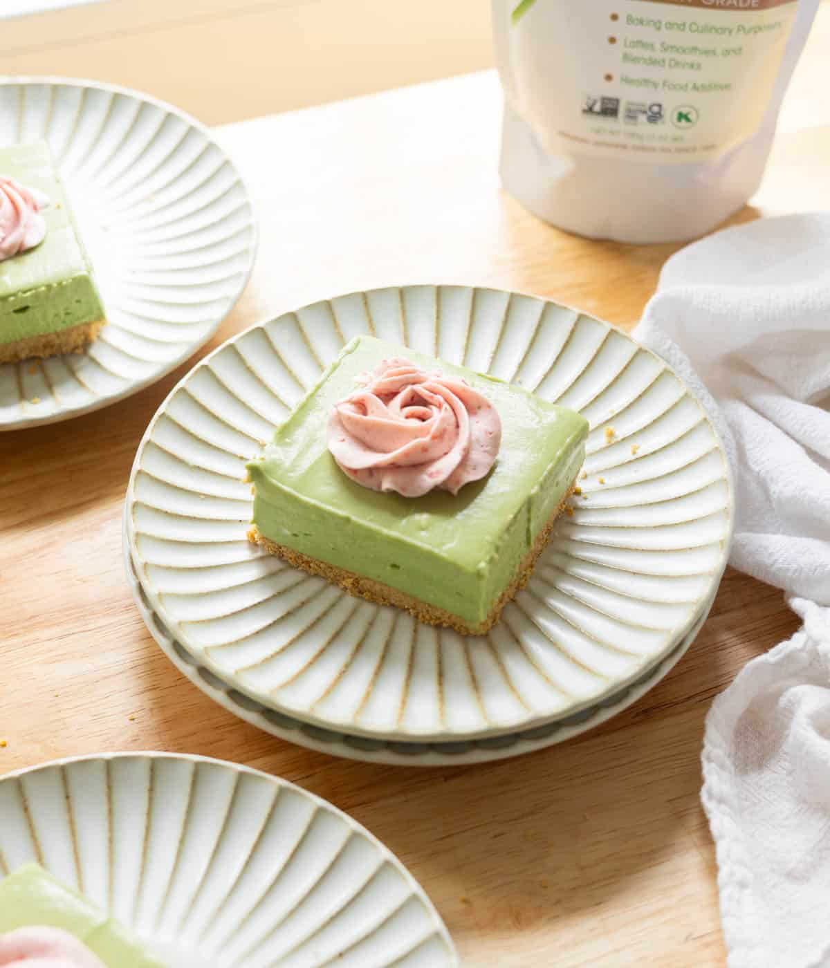 No bake matcha cheesecake bar topped with strawberry whipped cream on a fluted plate.