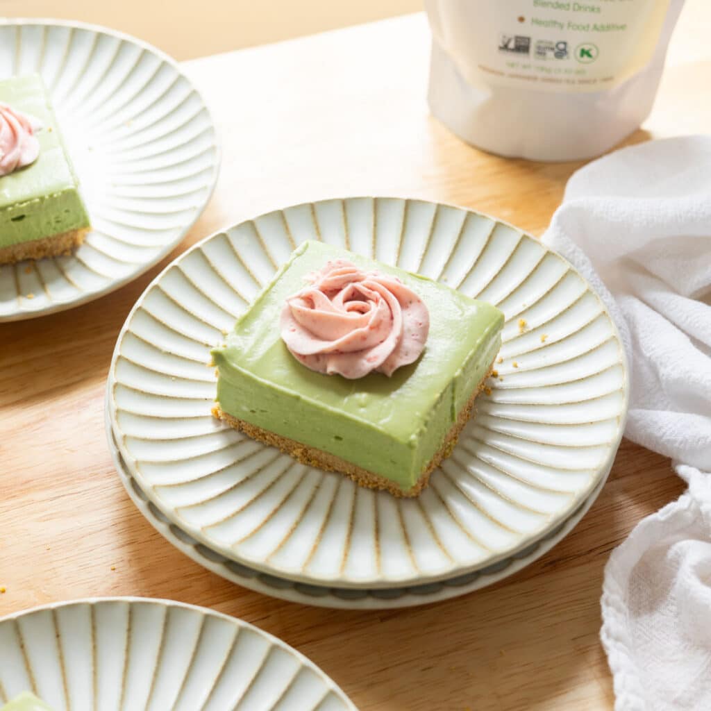 No bake matcha cheesecake bar topped with strawberry whipped cream on a fluted plate.