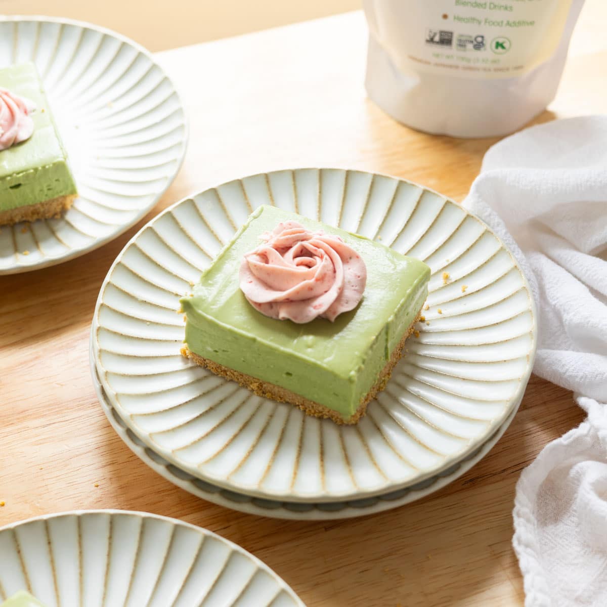 No bake matcha cheesecake bar topped with strawberry whipped cream on a fluted plate.
