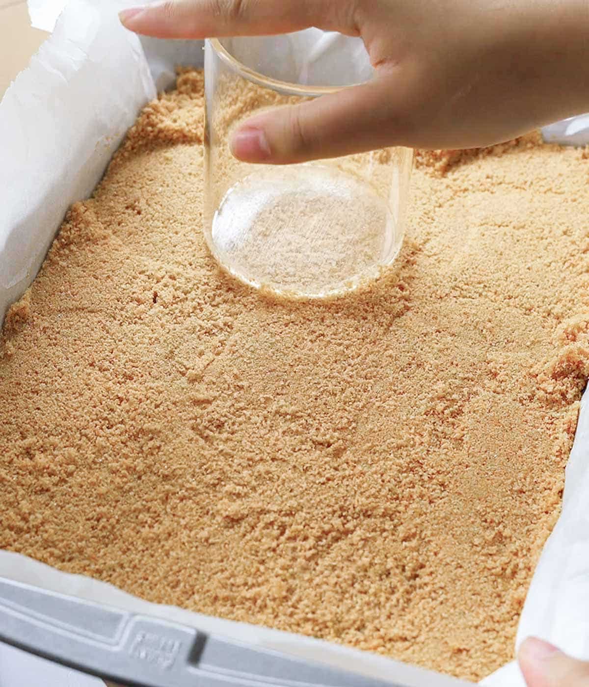 Pressing graham cracker crust into a 9x13-inch pan with the bottom of a glass cup.