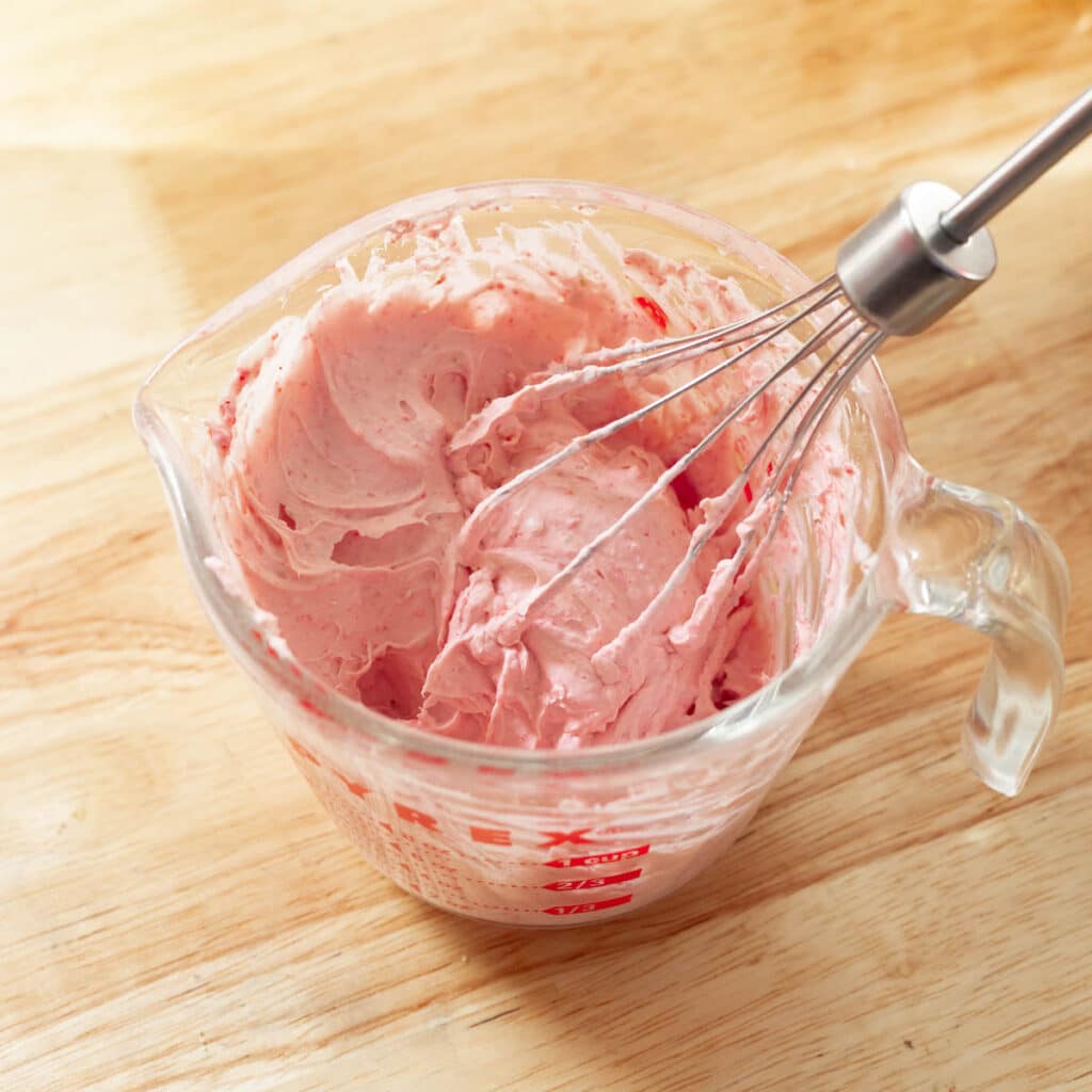 Pink strawberry whipped cream with stiff peaks in a measuring cup.