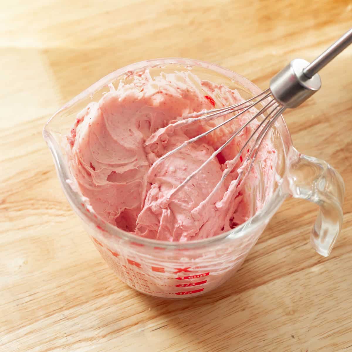 Pink strawberry whipped cream with stiff peaks in a measuring cup.