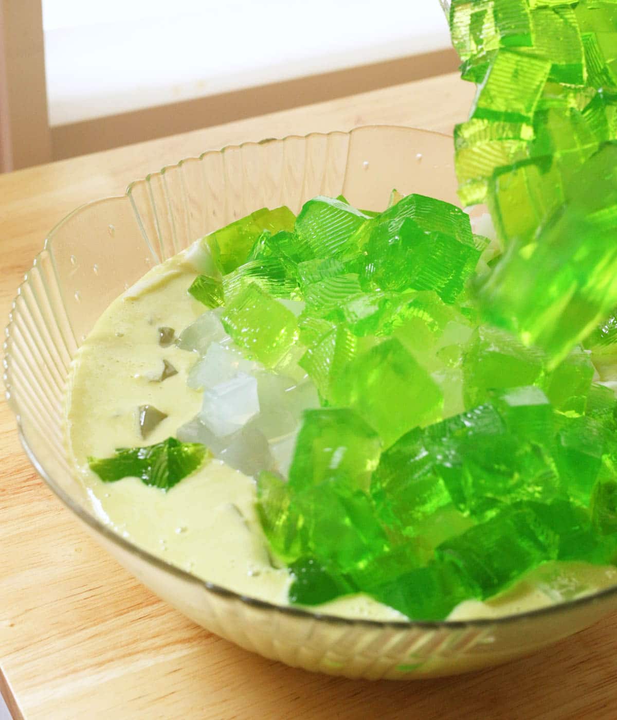 Adding set buko pandan jelly cubes into salad mixture in glass bowl.