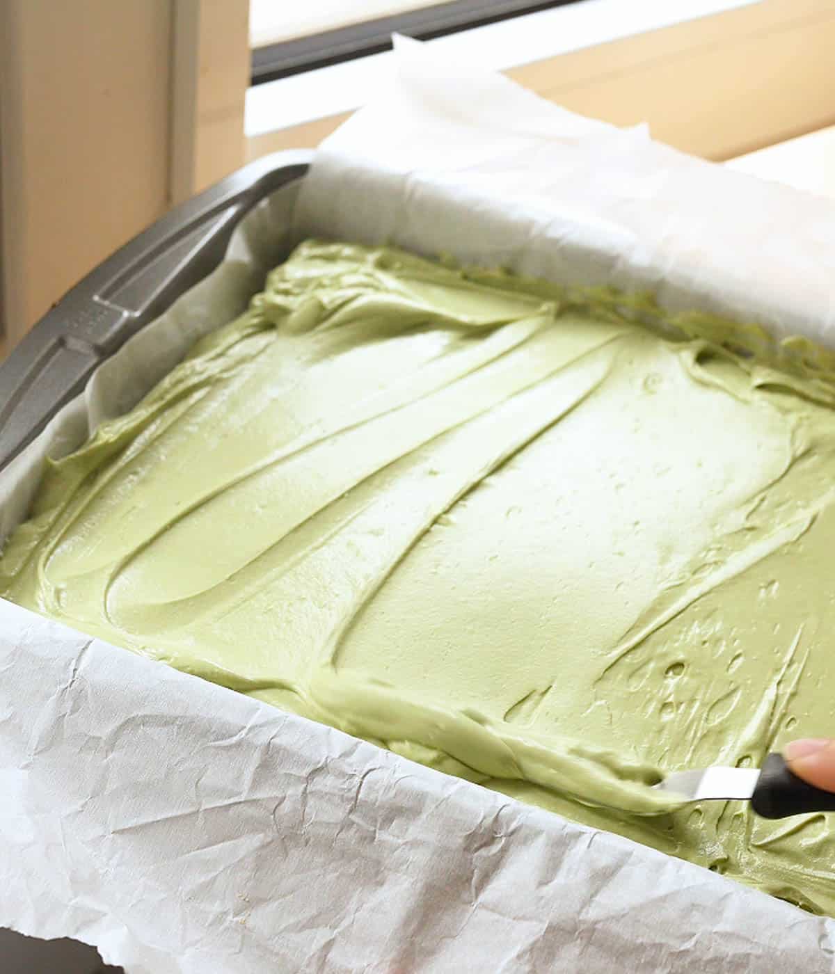 Spreading matcha cheesecake filling onto graham cracker crust.
