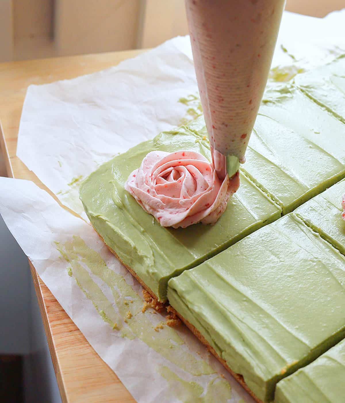 Piping a strawberry whipped cream rose on top of a matcha cheesecake bar.