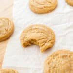 Corn sugar cookies spread across parchment paper, with a single bite taken from the center cookie.